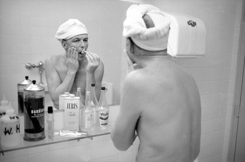 Entertainer Frank Sinatra shaving his face in a mirror.